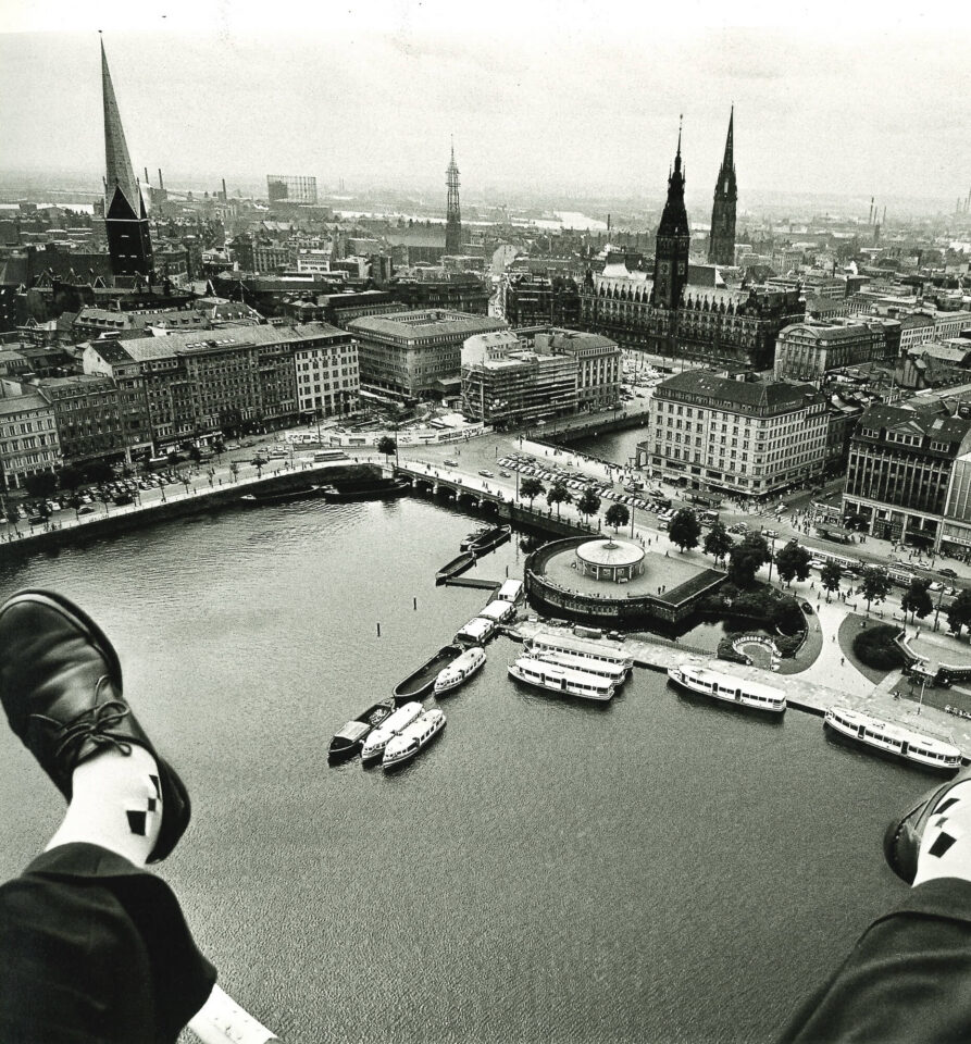 Zwischen den noch sichtbaren Füßen des Fotografen hindurch aus der Luft fotografiert: Innenalster, Jungfernstieg und das Hamburger Rathaus