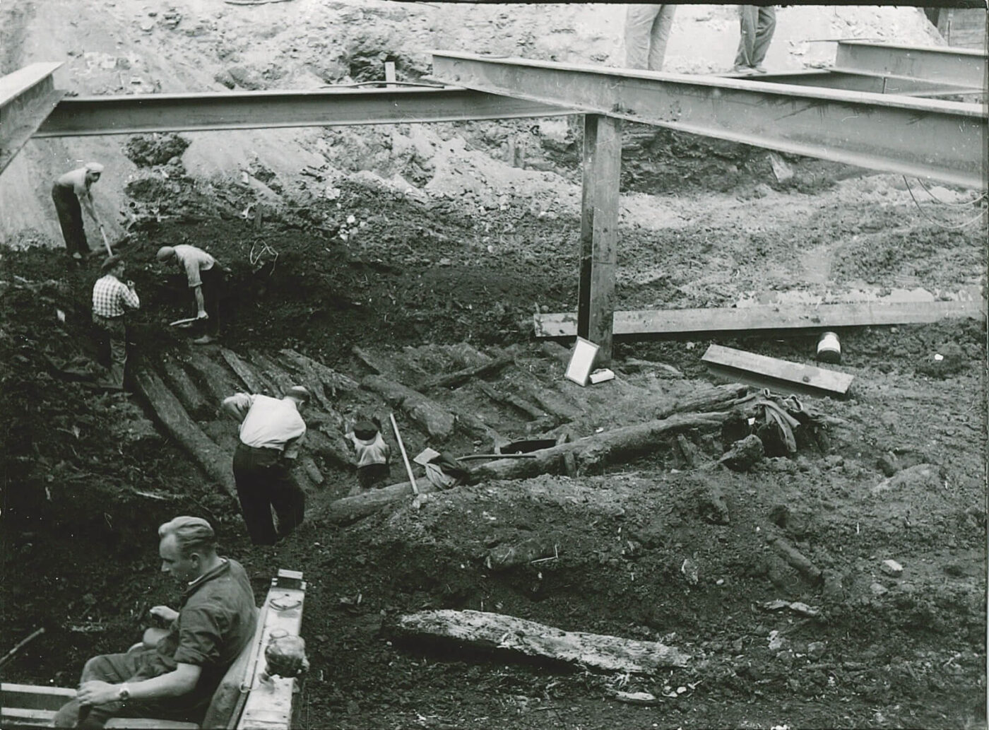 Foto der Grabungsarbeiten in den 1950ern. Arbeiter legen Fundamente aus Holzbalken frei.