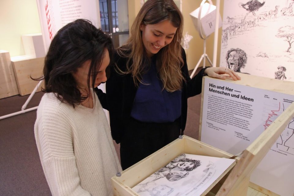 zwei Frauen in einer Ausstellung, sie betrachten eine Zeichnung in einer musealen Inszenierung