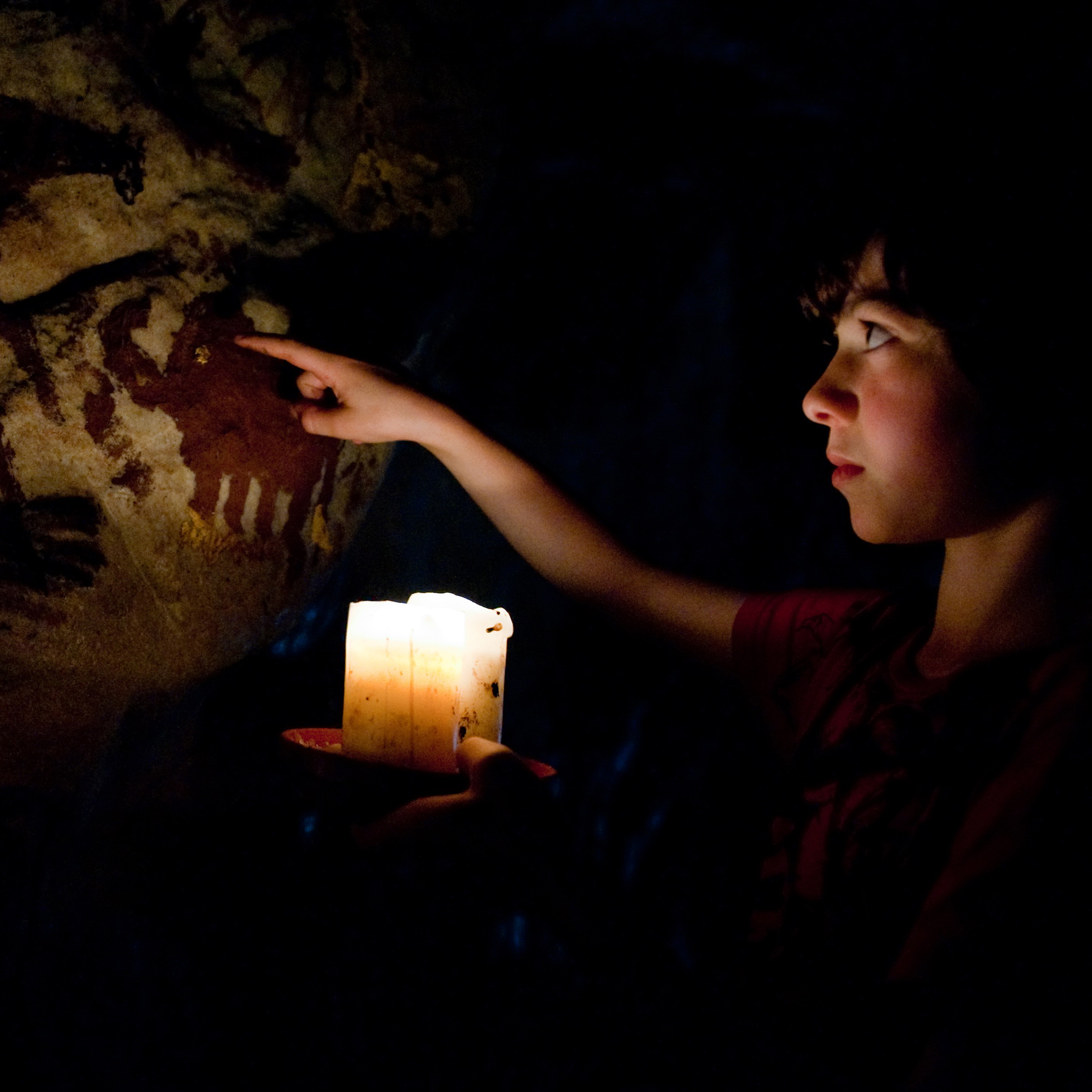 In der Steinzeithöhle beleuchtet ein Junge mit einer Kerze die bemalten Wände,