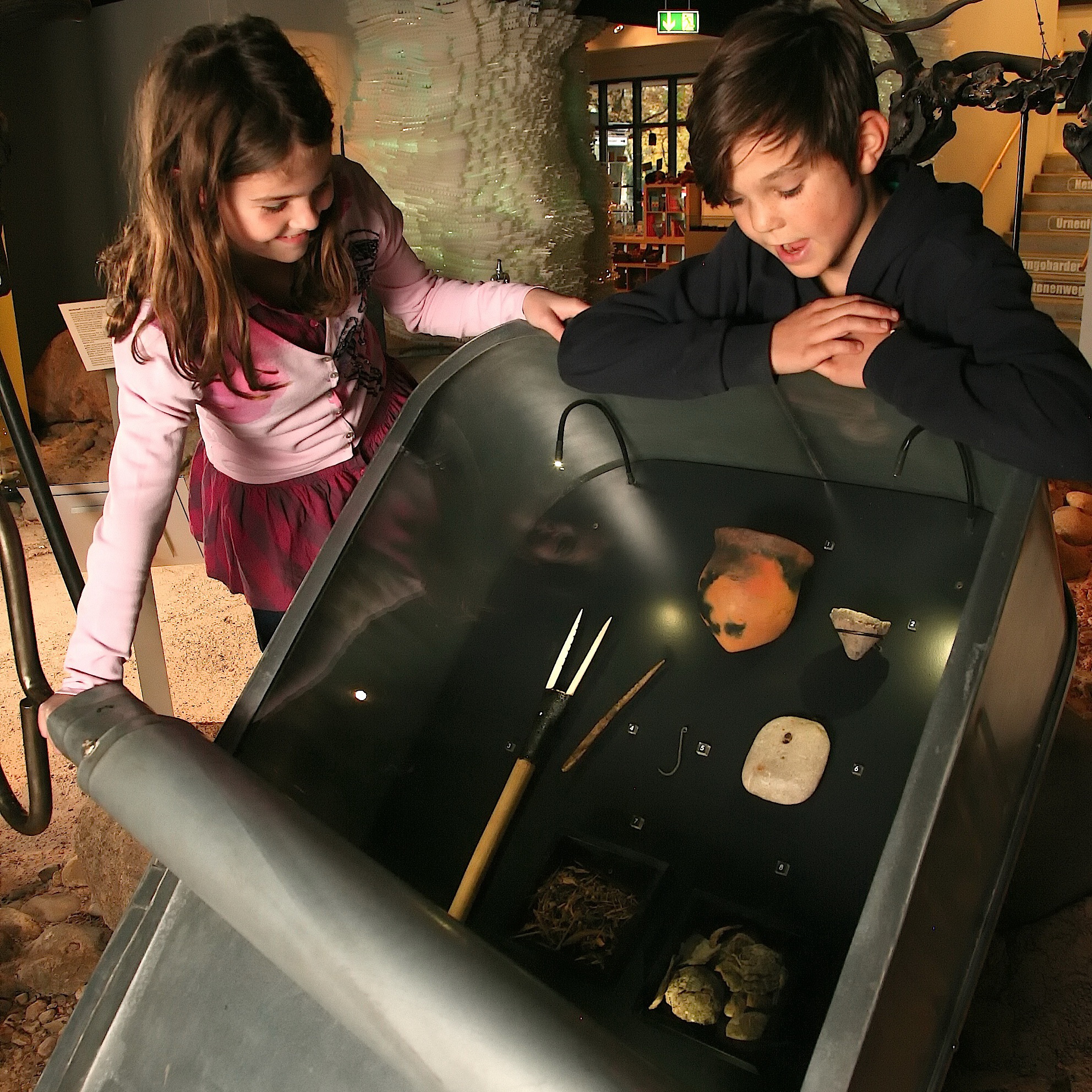 Zwei Kinder entdecken in der Ausstellung archäologische Funde.