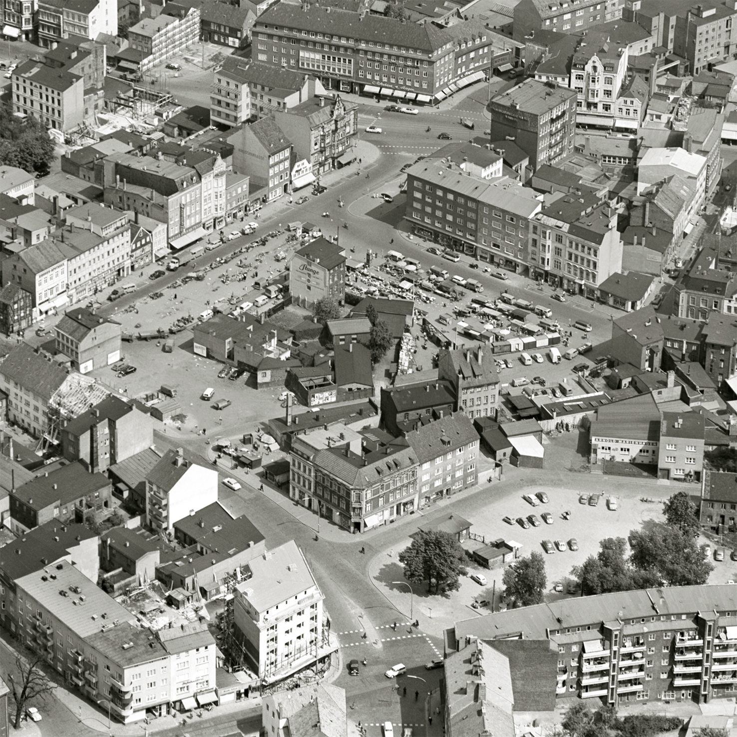 Das Foto zeigt eine Luftaufnahme vom 8. Mail 1959. Zusehen ist der Sand, Harburgs Marktplatz. Der Sand ist eine Institution und seit dem 17. Jahrhundert ein zentraler Ort städtischen Lebens. Im Zweiten Weltkrieg wurden Teile der südlichen Häuserzeile zerstört. 