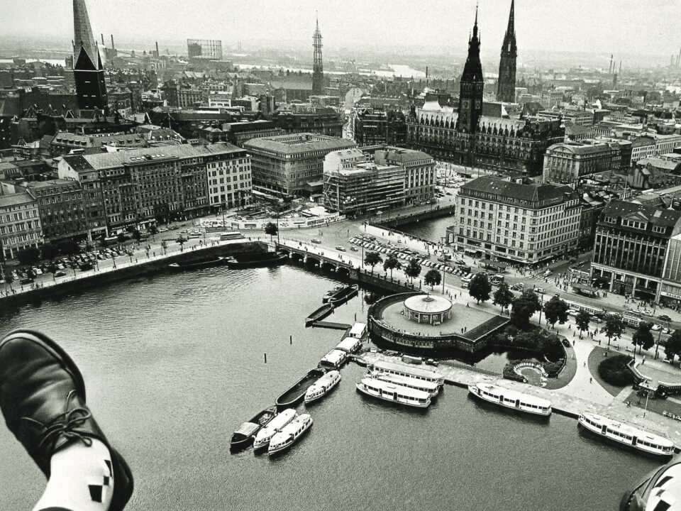 Zwischen den noch sichtbaren Füßen des Fotografen hindurch aus der Luft fotografiert: Innenalster, Jungfernstieg und das Hamburger Rathaus