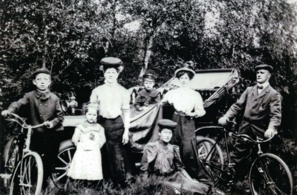 historisches Foto: vor einem Automobil posiert eine Gruppe (ein Mann, zwei Frauen und vier Kinder). Mann und ein Junge stehen neben Fahrrädern